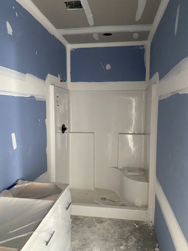 Modern bathroom with white vanity drawers, plastic protective covering, white painted ceiling, glass shower enclosure with black hardware, and tiled floor