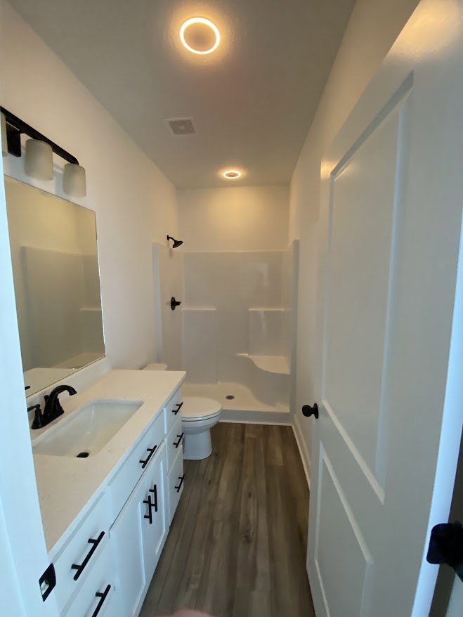 White bathroom featuring a black faucet on a white countertop, built-in drawers, and a close-up view of a toilet; circular light fixture overhead, tile walls, and modern cabinetry.