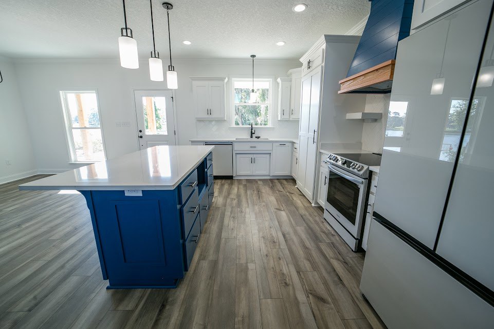 Kitchen with wood flooring, white cabinetry, white countertop island, stainless stove, large window, and recessed lighting