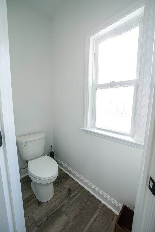 White toilet with lid up beside tiled wall in compact bathroom with plaster walls and small window.