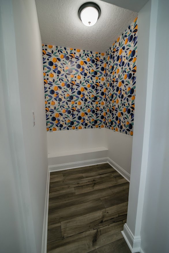 Hallway with wood flooring, white wall featuring a light switch, and patterned wallpaper on adjacent wall