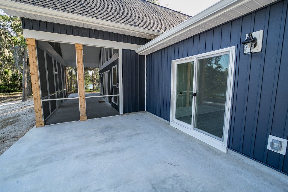 Blue-sided custom home with screened porch, sliding glass door, concrete floor, white electrical outlet, and nearby trees under a snowy sky