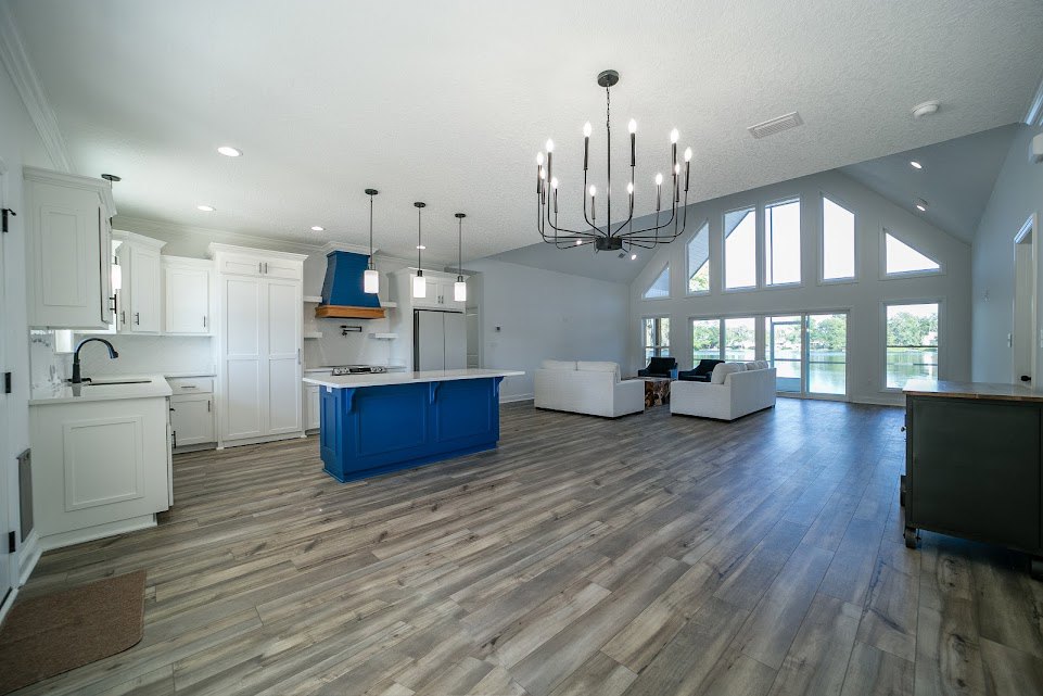 Open-concept kitchen and living area featuring a blue island with white countertops, white cabinetry, wood flooring, a chandelier hanging from the ceiling, white couch, and white