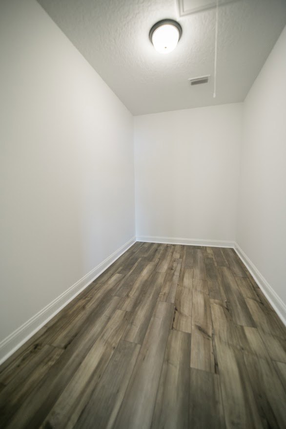 Wood flooring in a room with white plaster walls, ceiling-mounted light fixture, and minimalist interior design