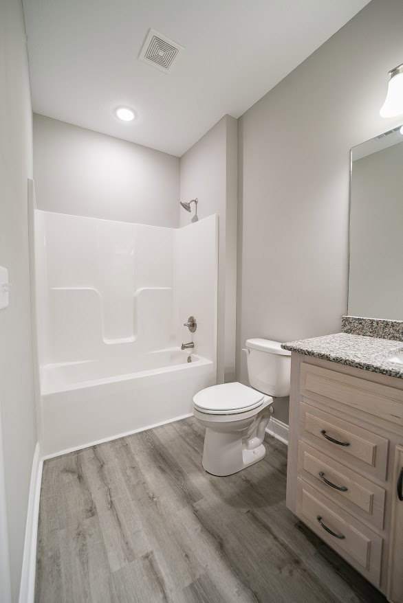 Modern bathroom with white toilet, built-in bathtub, light tile flooring, wall-mounted cabinetry, and neutral wall finishes