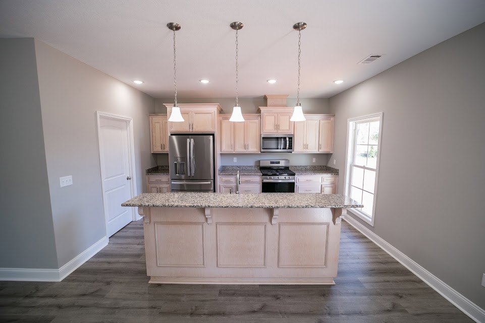 Granite island with undermount sink, stainless steel refrigerator, white cabinetry, gas range, and window with white trim in a modern kitchen