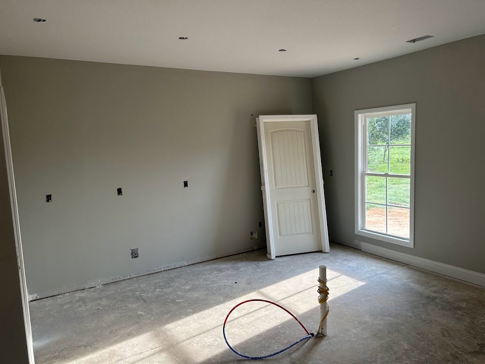 White plaster walls and ceiling, white door with round knob, window overlooking green grass, red and blue hoop and wire on light flooring