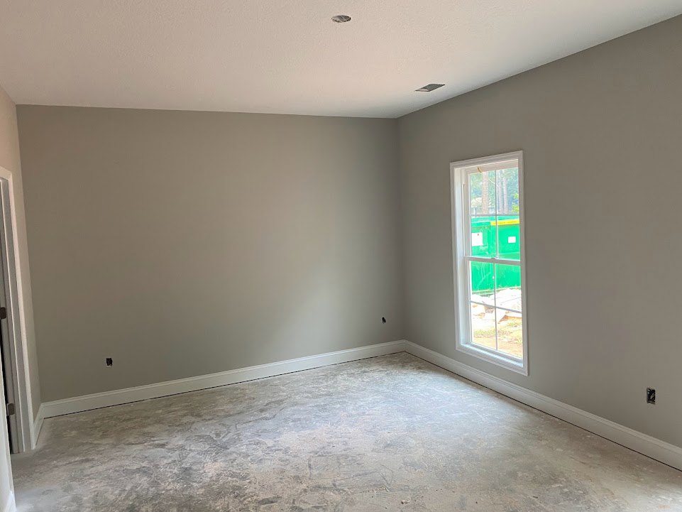 Concrete floor and white plaster walls in a minimalist room with a large window overlooking a green container.