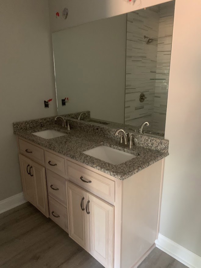 Bathroom with double sinks, expansive mirror, stone countertop, modern faucets, and light wood cabinetry