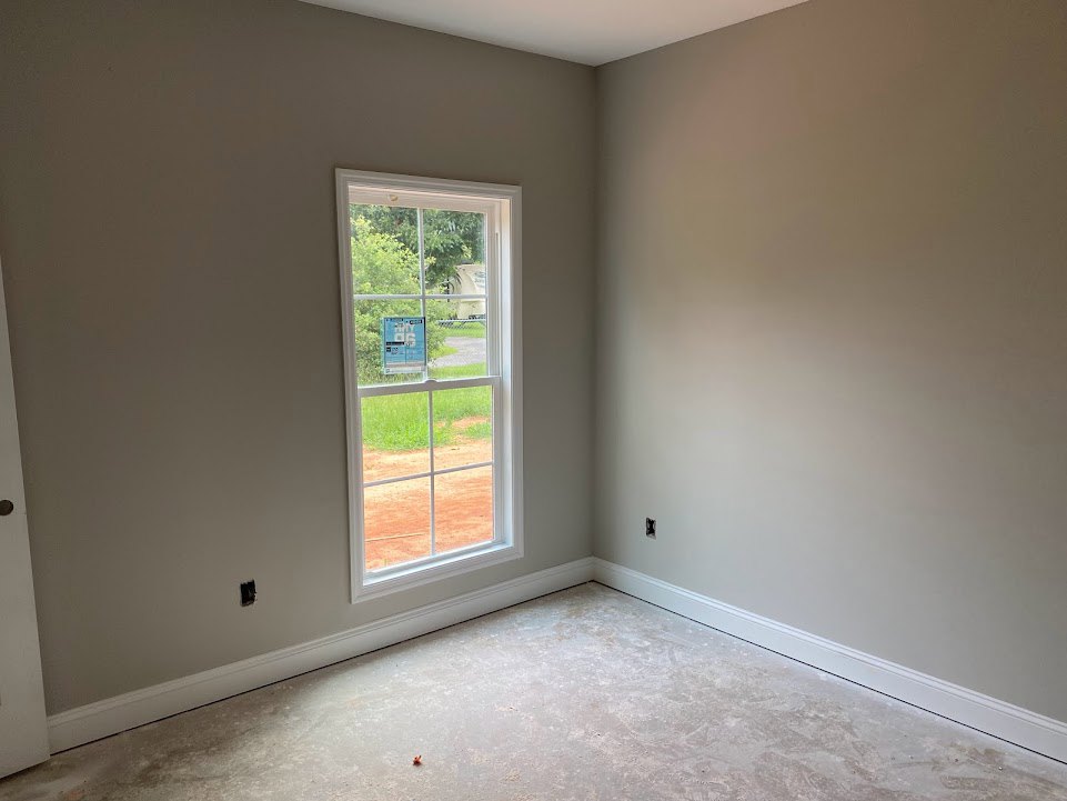 Concrete floor and white plaster walls in a room with a large window featuring a blue sign with white text.