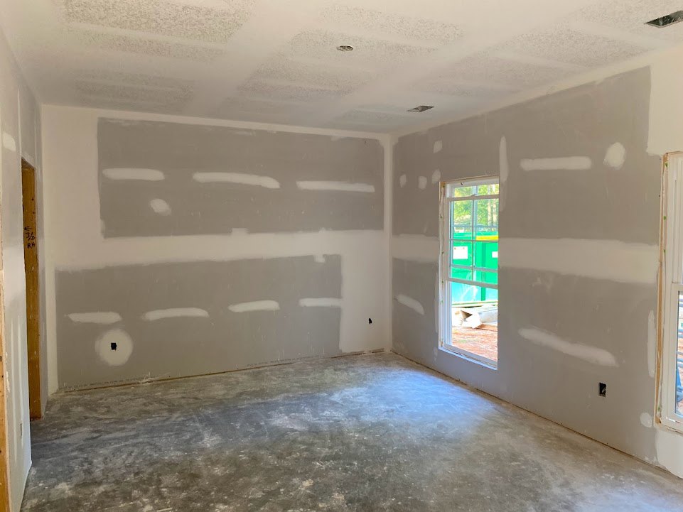 White-walled room with concrete floor painted white, large window facing a green wall, person painting one wall, black square artwork in a white circle displayed