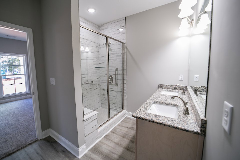 White bathroom with glass shower door, chrome handle, marble countertop, undermount sink, and wall-mounted light fixture
