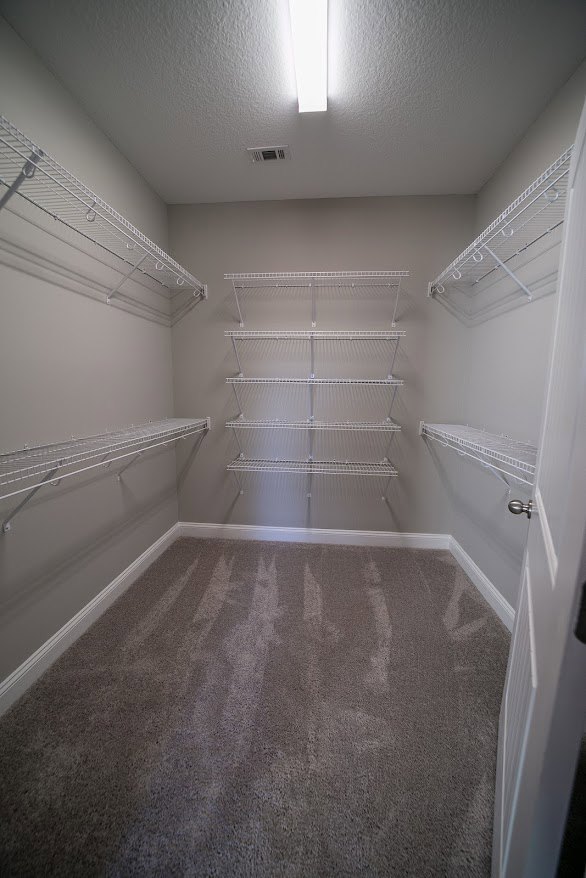 Spacious walk-in closet with white shelving, metal rods, built-in hooks, and light carpet flooring