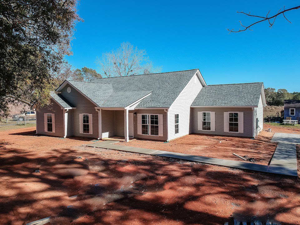 Two-story home with white trim, multi-pane windows, covered front porch, paved driveway, and mature trees under a clear blue sky