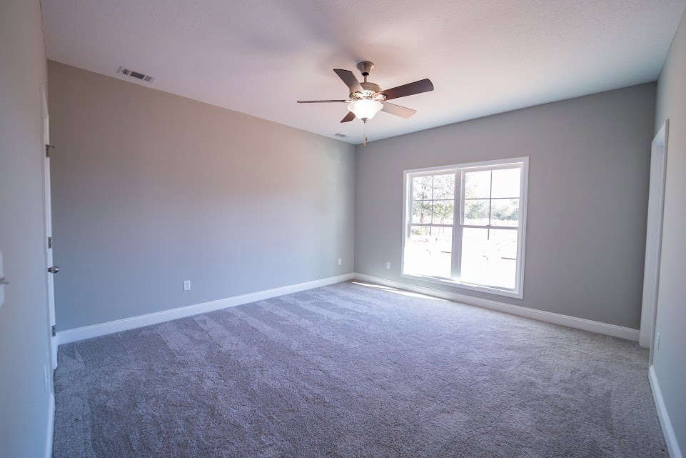 Carpeted room with white-framed window, ceiling fan with light fixture, neutral walls, and plaster ceiling