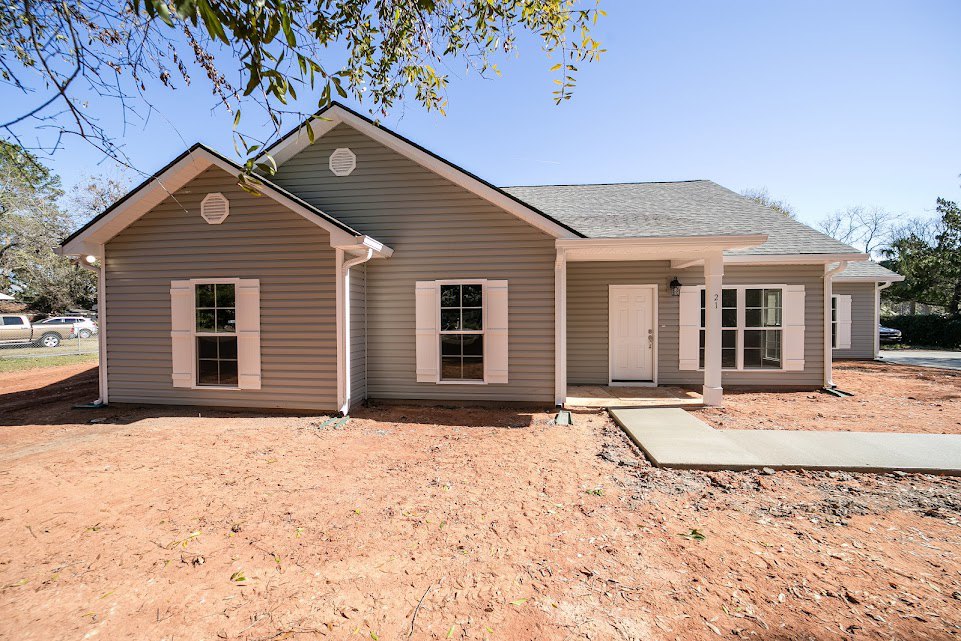 Single-story home with white door and multi-pane window, concrete porch slab, dirt yard, and white window frames.