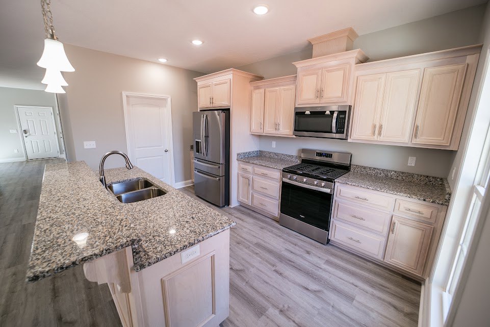 Granite countertops, stainless steel refrigerator, black-top stove, metal sink, white tree-shaped light fixture, wood cabinetry