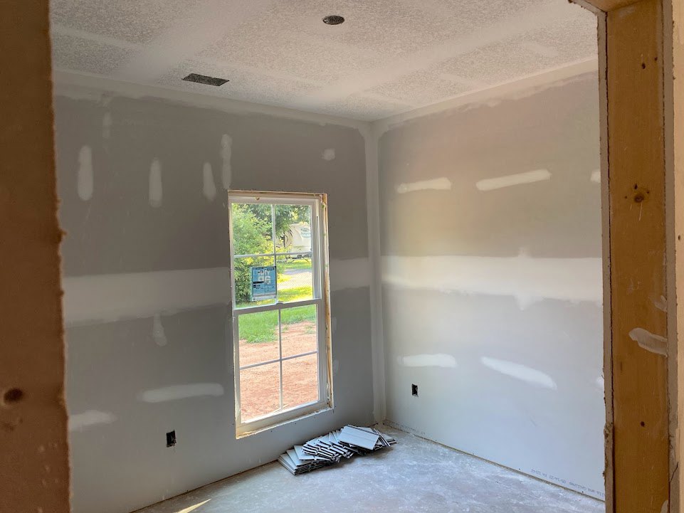 Bright room with two large windows, white painted walls, stack of white tiles on the floor, and smooth plaster ceiling.