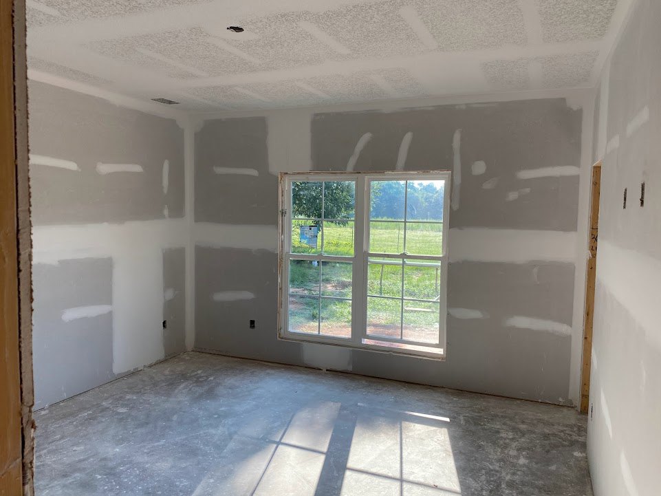 Sunlit room featuring a large window overlooking a grassy field, smooth concrete floor, white plaster walls, and minimalist ceiling detailing
