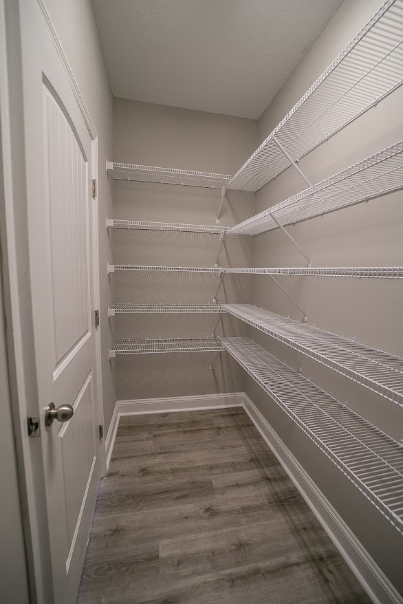 Closet with white built-in shelves, wood flooring with white baseboard trim, and a white door featuring a metal knob