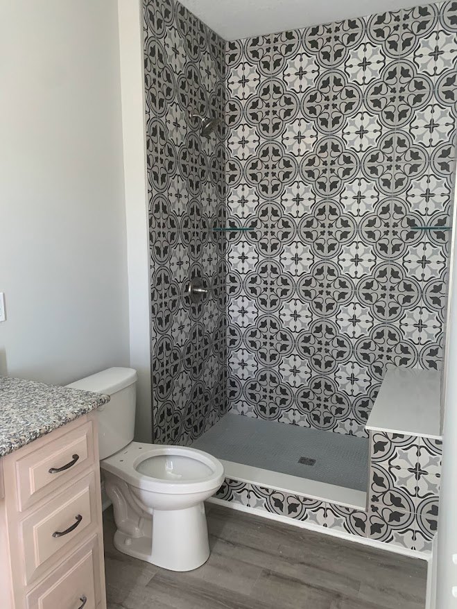 White countertop vanity with integrated sink, black and white tile shower wall, modern toilet, chrome fixtures, light wood drawer front, and neutral painted walls