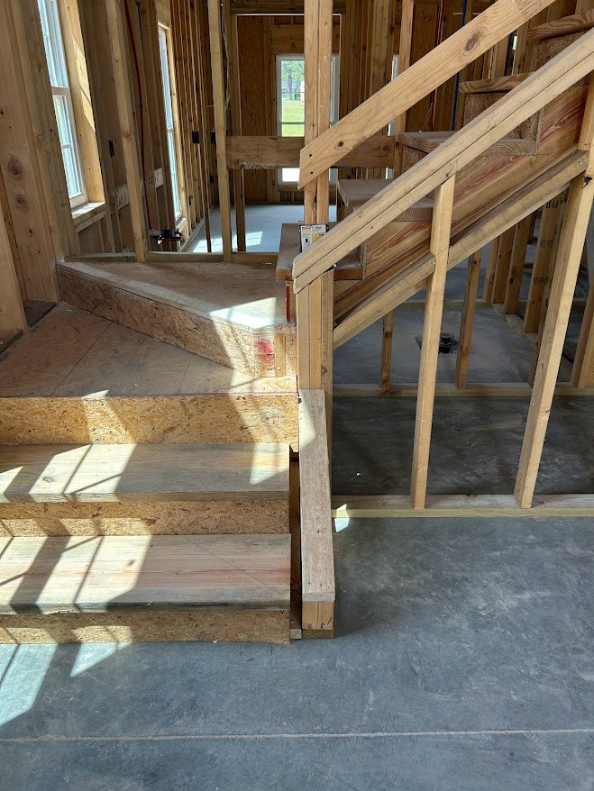 Hardwood staircase with open risers and wood railing, descending onto polished concrete floor in modern interior