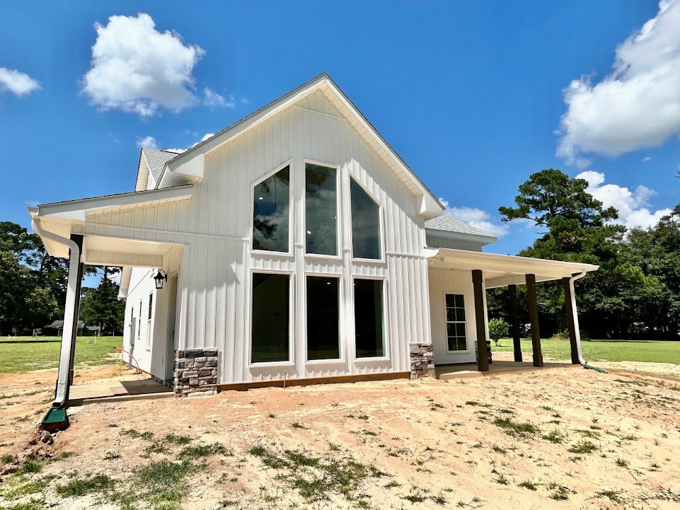 White siding house with large grassy yard, white framed windows, covered porch, brick foundation, and blue sky with scattered clouds