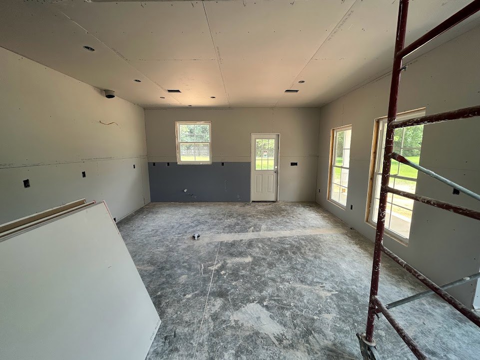 Bright room with white framed windows, glass paneled door, grey flooring, and a wooden ladder positioned near a wall; green lawn visible through window.