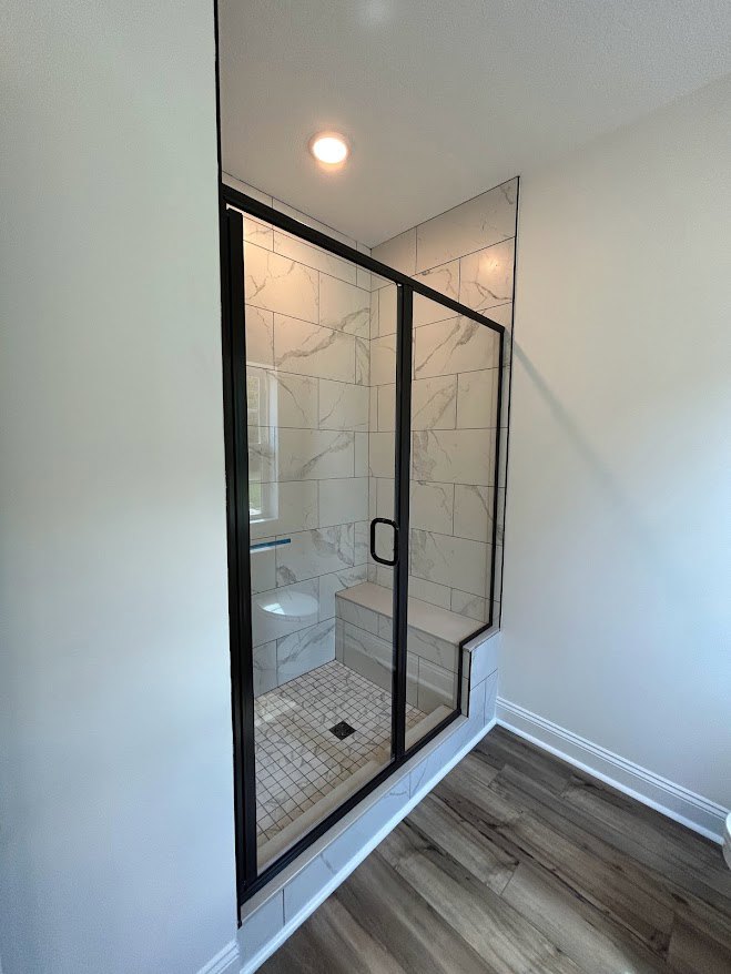 Tile shower with glass door and built-in bench next to white toilet, wood floor, plaster walls, and ceiling