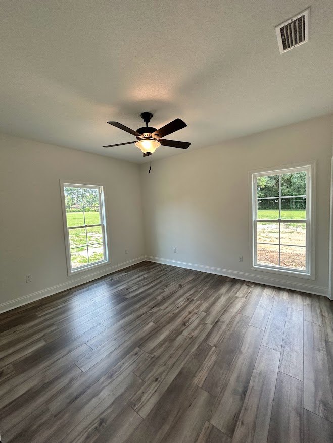 Wood flooring in a bright room with a ceiling fan, recessed ceiling vent, and large windows overlooking a grassy field