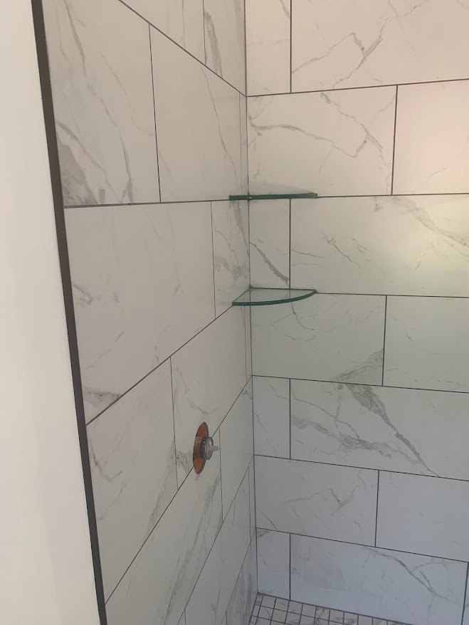 White tile shower wall with black grout, glass shelf mounted above a cracked tile, black line detail visible on white surface.