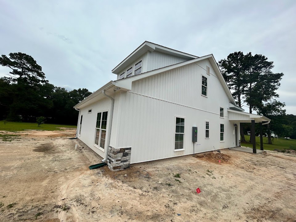 White house with white-framed windows, brick and stone fence, large tree in the yard, and trees in the background