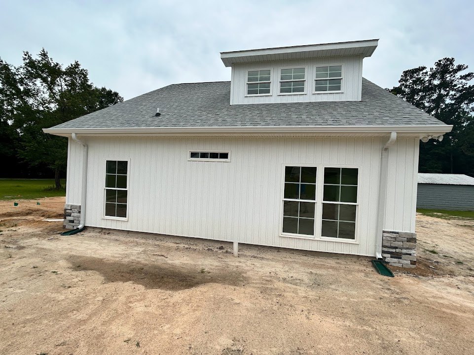 White house with white-framed windows, gray roof, and unfinished dirt yard in front.