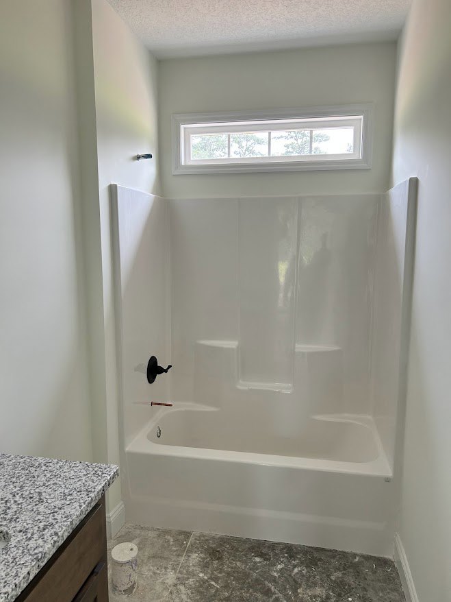 Freestanding white bathtub beside a speckled black and white countertop, white-framed window, and tiled bathroom walls