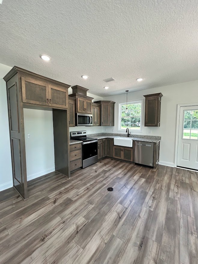 Kitchen with wood flooring, black and silver oven, white door with window, circular object on floor, window with natural light, close-up of stainless steel dishwasher, white