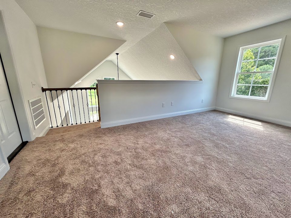 Open living area featuring a carpeted floor, white walls with white trim, staircase with modern railing, large window overlooking trees, and grey rectangular accent with white