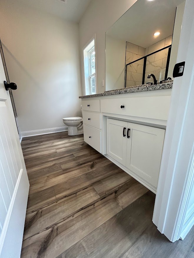 Bathroom with white toilet, wood flooring, white cabinets, and a rectangular sink with chrome faucet