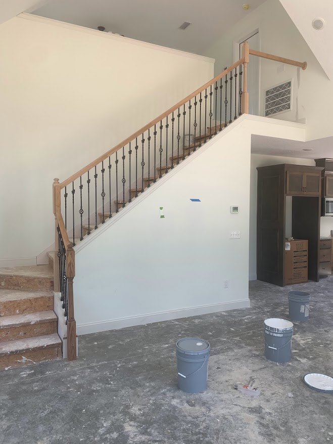 Wood staircase with black metal railings, light plaster walls, brown cardboard box and grey bucket on unfinished floor