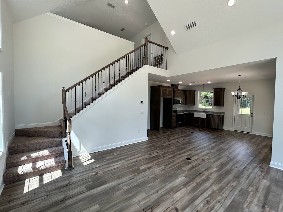 Hardwood flooring and white walls in a foyer with a metal-railed staircase, glass-paneled white door, and window letting in natural light