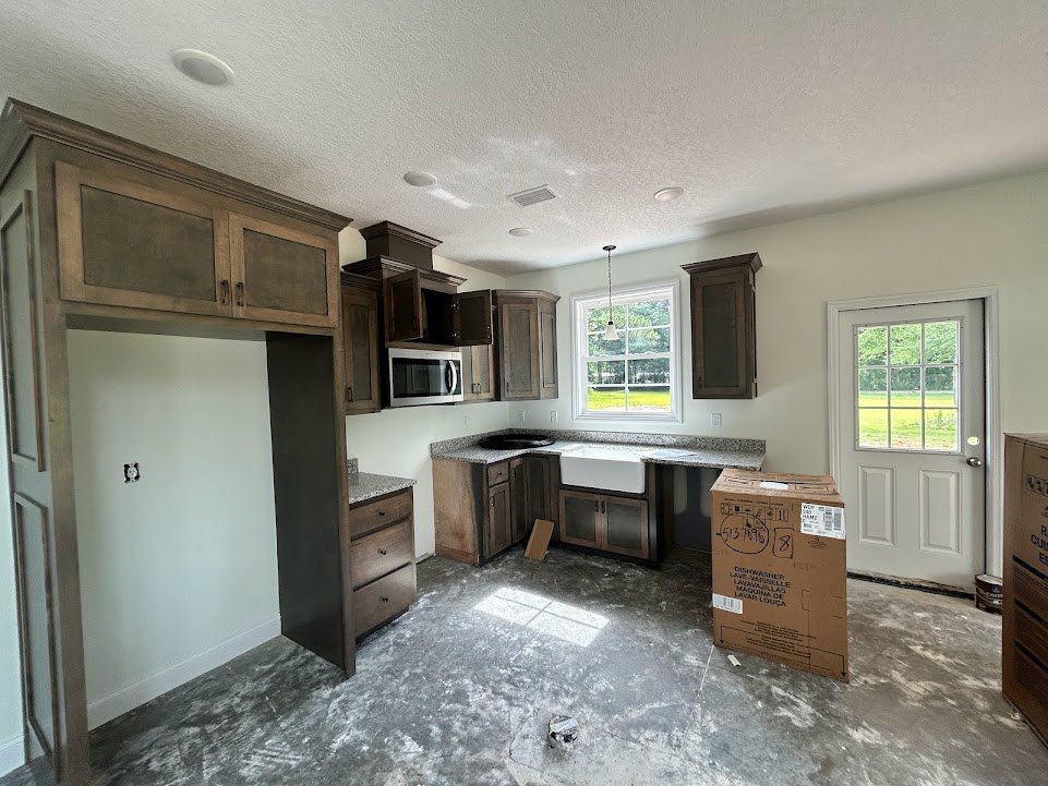 Modern kitchen with white cabinetry, stainless microwave oven, brown cardboard box on countertop, white door with glass window, overhead ceiling light, wood flooring