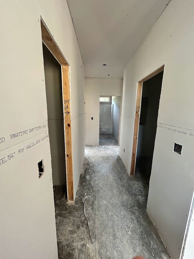 Hallway with white plaster walls, open wood-framed door, wood trim, and visible wood beam with black writing