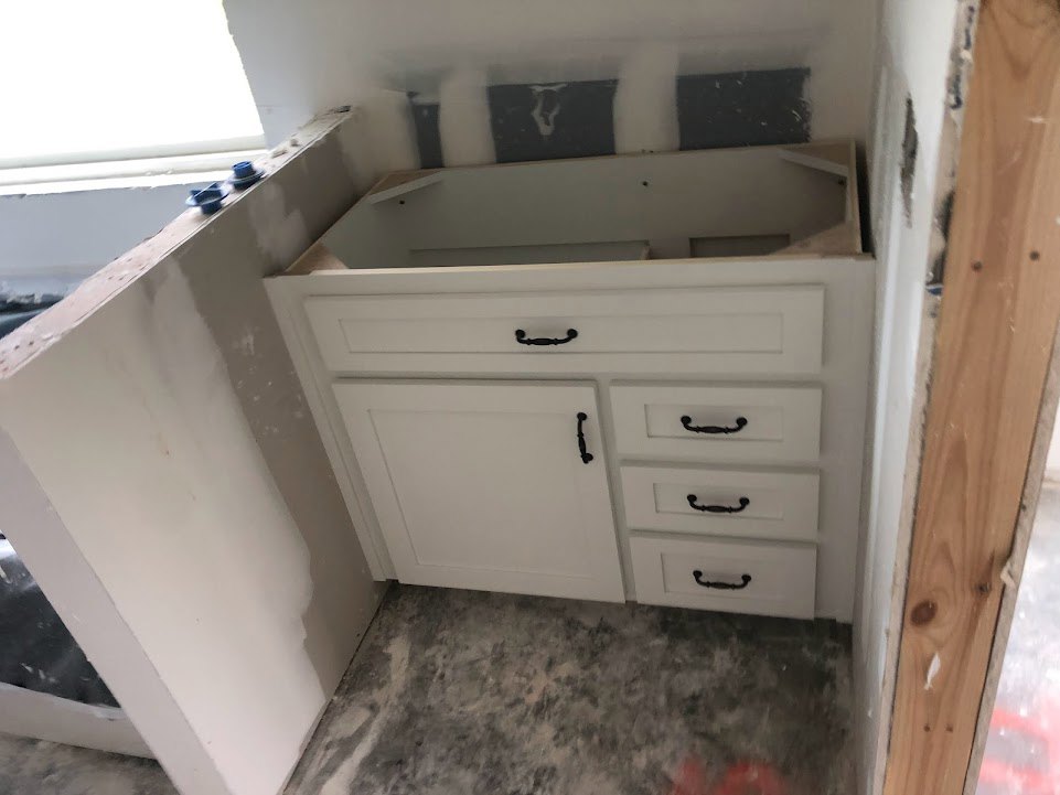 White shaker cabinets with black handles, stainless steel sink set into quartz countertop, light wood flooring, person standing beside painted wall.