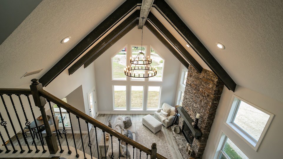 High angle view of living room with white chair and pillow, couch with pillows positioned on stairs, white ottoman on carpet, rectangular window on wall, visible molding and stair