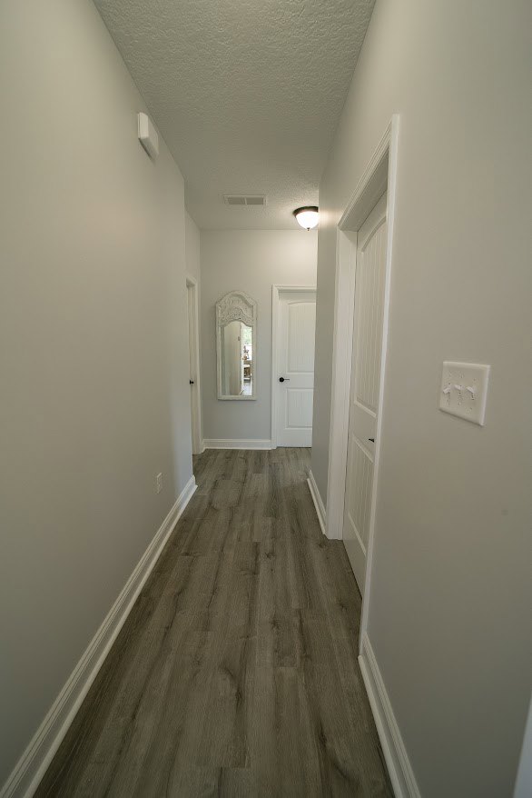 Hallway with light wood flooring, white plaster walls, large wall mirror, and white doorway
