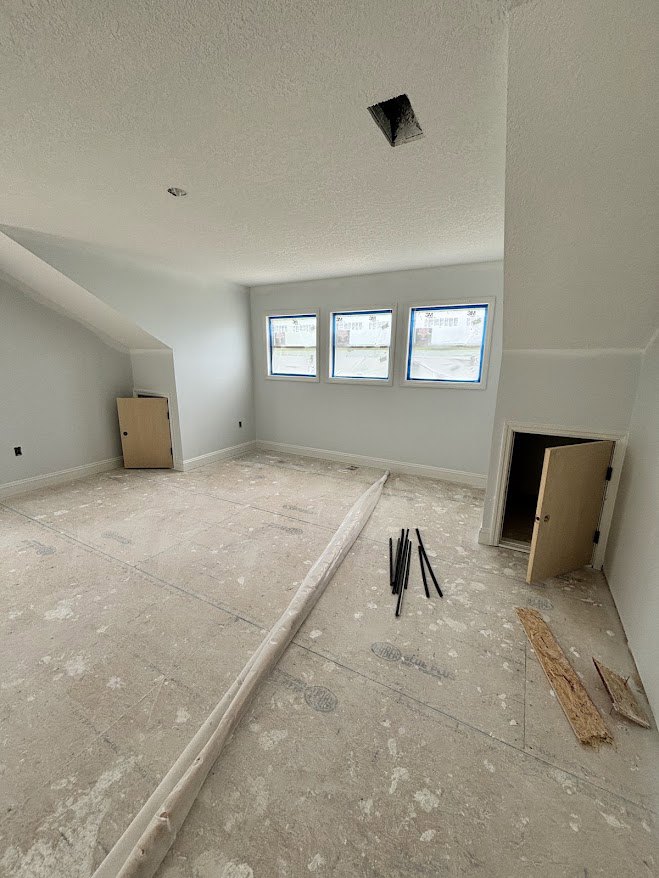 White plaster walls and floor, blue-trimmed windows, black door handle, wood plank resting on concrete floor
