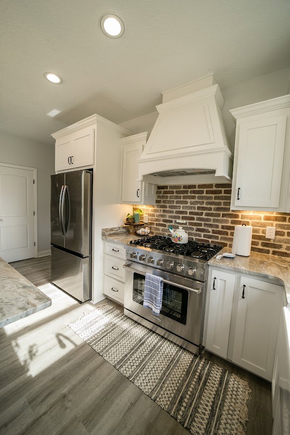 Modern kitchen featuring stainless steel stove with oven, refrigerator, white cabinetry, stone countertops, and light wood flooring