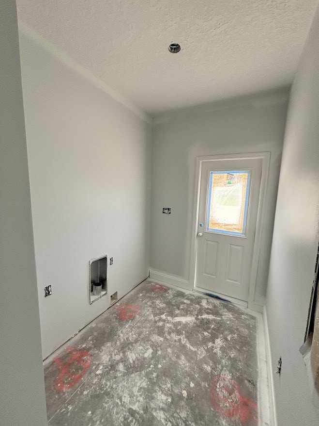 Concrete floor with scattered red markings, white door featuring a window, plaster walls, exposed ceiling hole, and a red and gray object marked with an X.