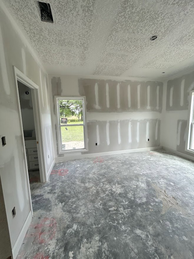 White walls and ceiling, large window with a sign, grey flooring with red paint marks, black rectangular object on white surface