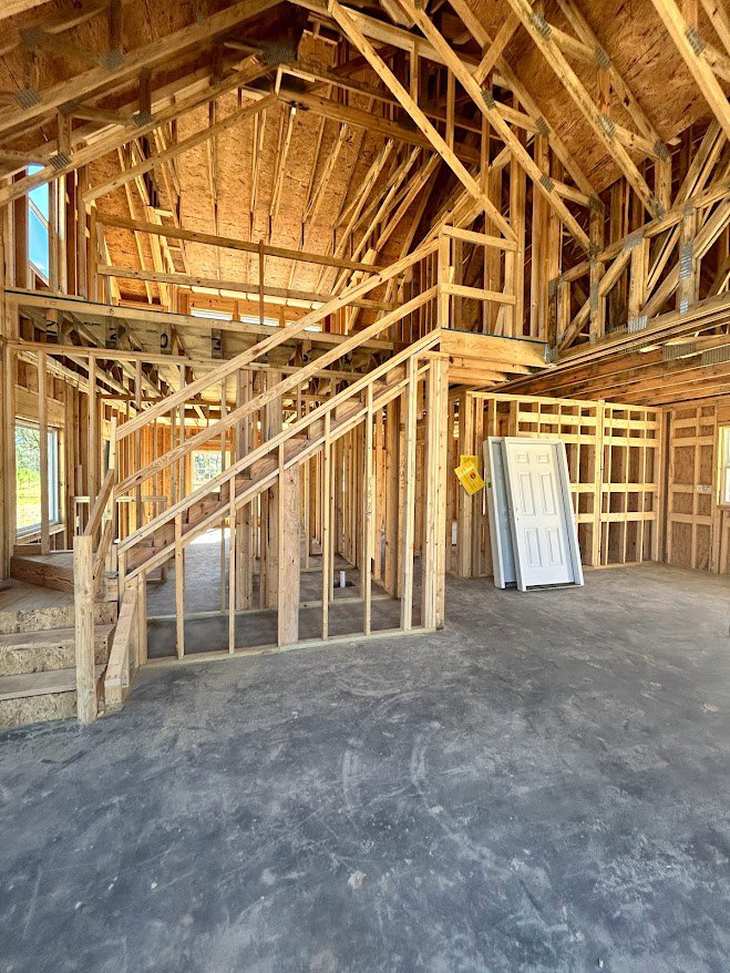 Unfinished interior with exposed wooden beams, concrete floor, white door, and partially built staircase
