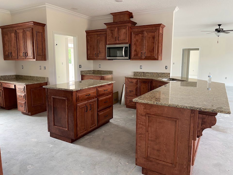 Granite countertops and wood cabinets in a kitchen with a marble-topped island, stainless steel microwave, ceiling fan with light, drawers beneath counters, and tile flooring